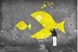 En bild på en graffitivägg där en stor fisk äter upp en liten.
