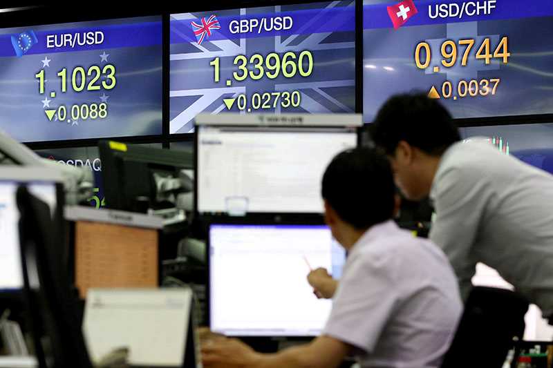 Två män vid ett skrivbord och i bakgrunden visas skärmar med valutakurser för euro/dollar, pund/dollar och schweizerfranc/dollar.