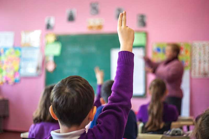 En pojke räcker upp handen i ett klassrum